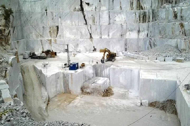 Heavy machinery operating within a large, blocky Carrara marble quarry.